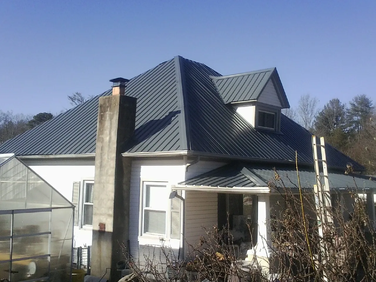 Dark blue standing seam metal roof on a white farmhouse with dormer — Slate & Tile Roof Repair by Roofing Brothers in Alton