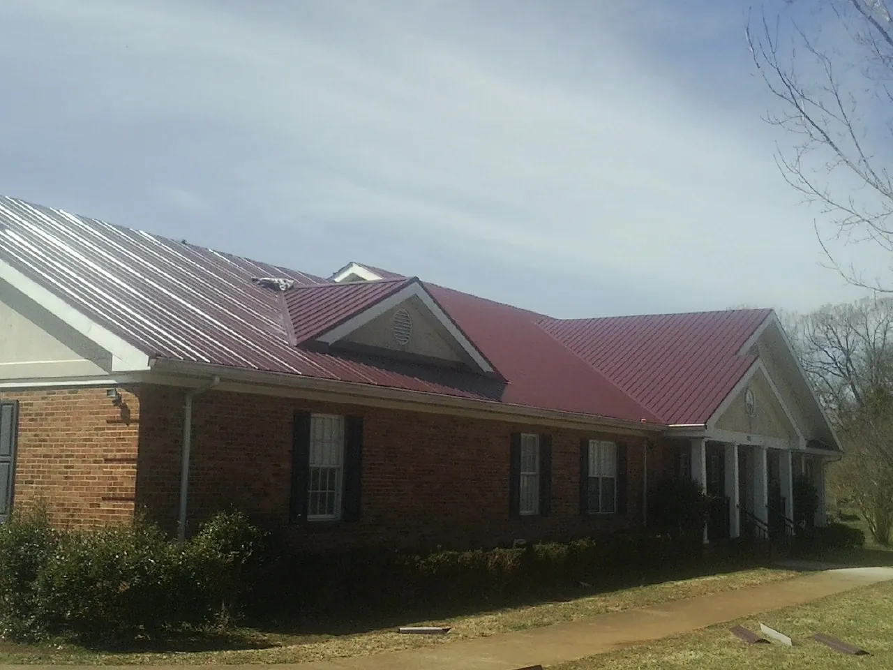 Red metal roof with gabled entries on a long brick building, from a Hail Damage Roof Repair job in Alton